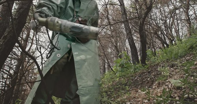Low angle unrecognizable guy in hazmat suit and gas mask searching for radiation with Geiger counter in abandoned forest near Chernobyl.