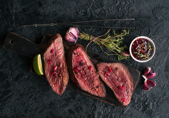 Beef steaks with pomegranate seeds, vegetables and thyme on a black slate table. The view from the top.