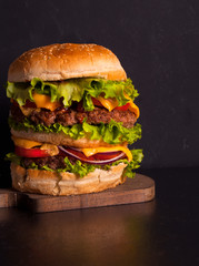 A large rustic Hamburger on a dark wooden table. Fast food. Copy space