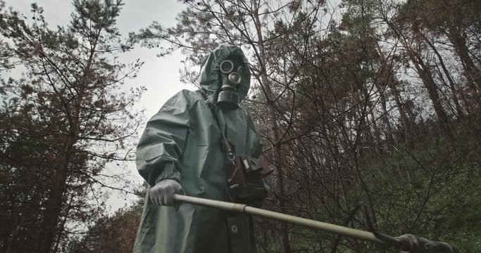 Tracking shot of anonymous male in hazmat suit and gas mask swinging Geiger counter over ground while walking in dead forest near Chernobyl.