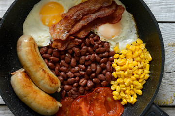 English breakfast - sausages, corn, eggs, bacon, beans and fresh tomatoes in a griddle