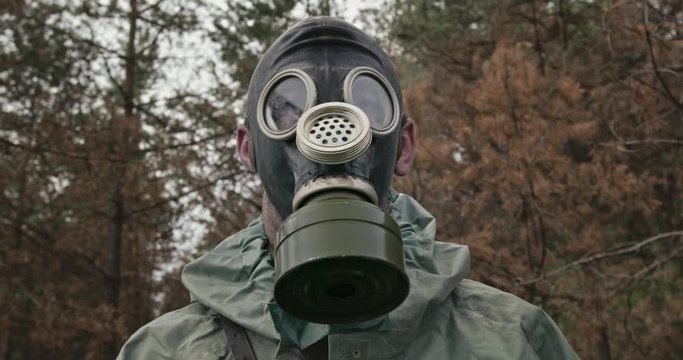 Man in hazmat suit putting on gas mask in forest