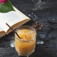 Iced cold coffee on an old wooden table with a book. Summer morning
