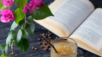 Iced cold coffee on an old wooden table with a book. Summer morning