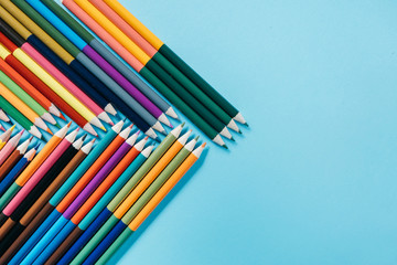 School concept. Closeup images of many color pencils on blue background. Flat lay, top view, copy space.