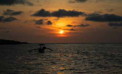 Sunset over calm ocean with balinese boat