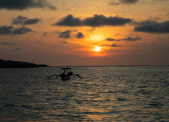 Sunset over calm ocean with balinese boat