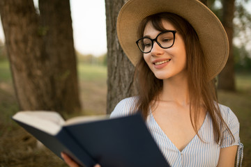 Young woman in the park is reading a book. Sit under a tree on a soft rug