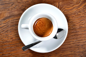 A cup of coffee (espresso) with a spoon on a wooden table