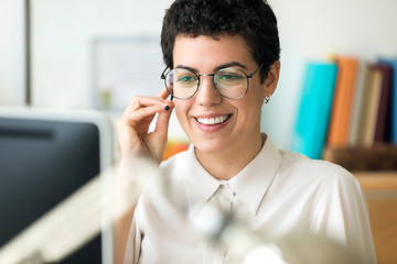 Smiling young business woman using her free hands to make a call while working with her computer in...