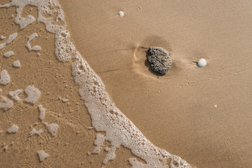 Abstract sand background with lying stone and bubbling ocean water.