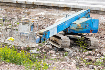 Fototapeta premium Old abandoned tracked articulated boom rusty crawler in the middle of the street. Outdated construction and working equipment and transport. Construction professional abandoned machinery. Industrial.