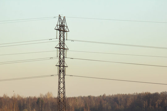 Minimalistic image of the metallic construction of the pylon of the high-voltage power line against the evening blue sky and forest. Distribution and transmission of electricity and voltage industry.