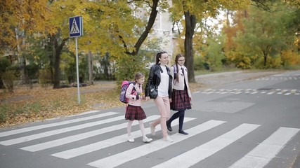 Mother with her daughters are going to school cross the road at a pedestrian crossing.