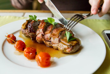 A restaurant visitor punctures a piece of duck roll in demi-glace sauce in a plate on the table