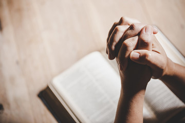 Spirituality and religion, Hands folded in prayer on a Holy Bible in church concept for faith. - obrazy, fototapety, plakaty