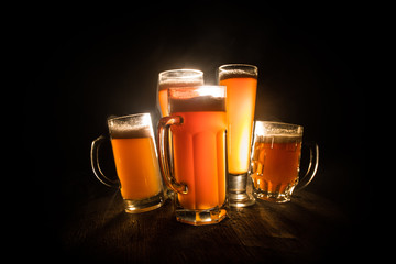 Creative concept. Beer glasses on wooden table at dark toned foggy background.