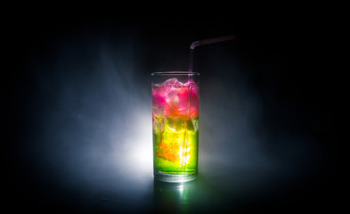 Cocktail glass splashing on dark toned smoky background or colorful cocktail in glass. Party club entertainment. Mixed light.
