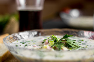 Cold Soup Okroshka. With sausage, vegetables and kvass serving size in bowl and raw ingredients on wooden table