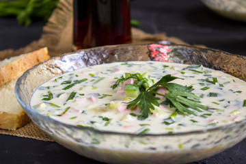 Cold Soup Okroshka. With sausage, vegetables and kvass serving size in bowl and raw ingredients on wooden table