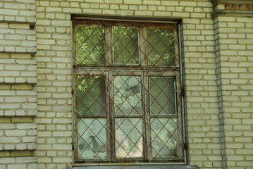 one old window behind an iron grate on a brown brick wall 