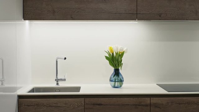 Stylish compact modern built-in kitchen with sink and glass-topped hob decorated with a blue glass vase of fresh yellow and white spring tulips.