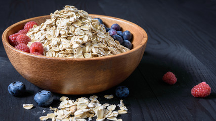 oatmeal with blueberries and raspberries in a wooden bowl on a black wooden table