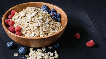 oatmeal with blueberries and raspberries in a wooden bowl on a black wooden table