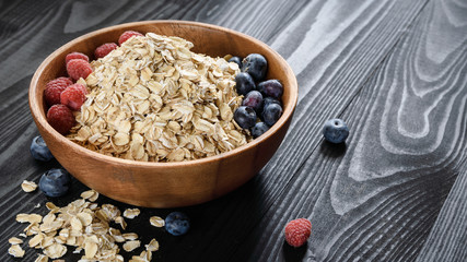 oatmeal with blueberries and raspberries in a wooden bowl on a black wooden table