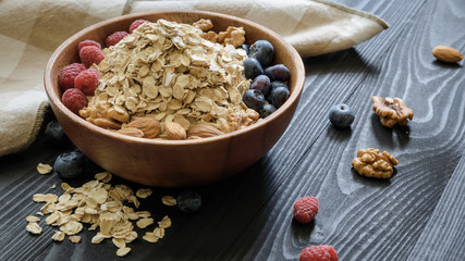oatmeal with blueberries, raspberries, almond and walnuts in a wooden bowl on a black wooden table
