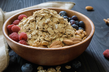 oatmeal with blueberries, raspberries, almond and walnuts in a wooden bowl on a black wooden table