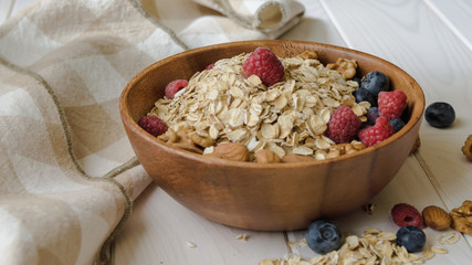 oatmeal with blueberries, raspberries, almond and walnuts in a wooden bowl on a black wooden table