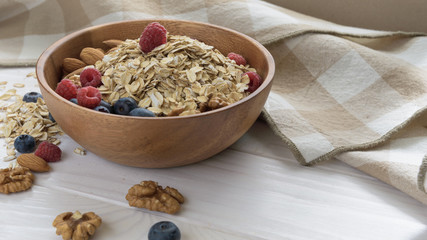 oatmeal with blueberries, raspberries, almond and walnuts in a wooden bowl on a black wooden table