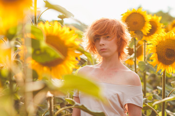 young girl enjoying nature on the field of sunflowers at sunset, portrait of the beautiful redheaded woman girl with a sunflowers in a sunny summer evening