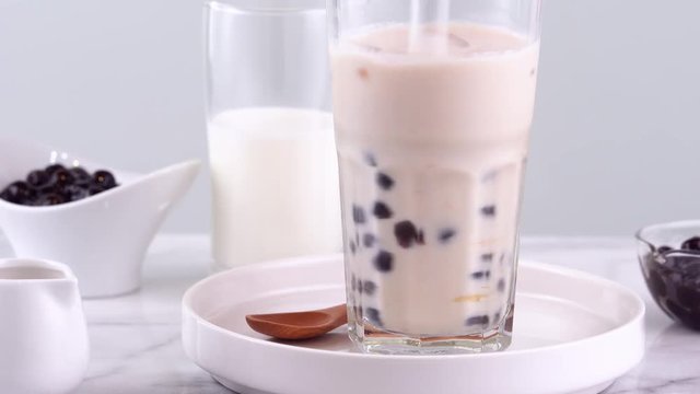 Stirring tasty taiwanese popular drink tapioca pearl bubble milk tea in glass cup on bright marble table white tray, homemade concept. 4K shot video