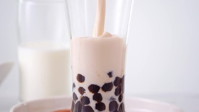 Slow motion - pouring milk tea in glass cup with tasty popular taiwan tapioca pearl bubble on bright marble table and white tray. 4K video shot.