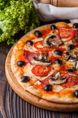 Pizza with tomato, olives, champignons, ham and cheese on round wooden plate
