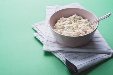 Oatmeal in a pink plate with a spoon on a white cloth, green background