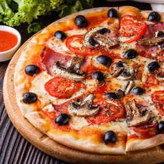 Pizza with tomato, olives, champignons, ham and cheese on round wooden plate
