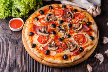 Pizza with tomato, olives, champignons, ham and cheese on round wooden plate