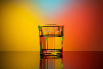 Art glitch effect, glass glass with water on a bright multi-colored background, minimalism