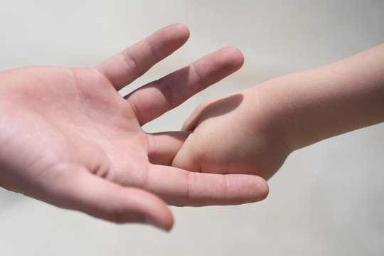 Closeup of two touching hands of small baby boy holding finger of male father as symbol of family love and trust on blurred background. Help and support for the child. Reliable adult. Parent. Father.