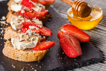 Bruschetta with strawberries, blue cheese, walnut and honey on stoyn plate