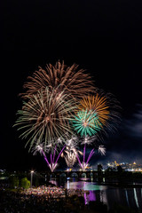 Imagen vertical de mucha gente observando los fuegos artificiales sobre el puente en el r&iacute;o con la ciudad vieja al lado