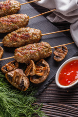 Shish kebab on the skewers with sauce, grilled mushrooms on rustic table