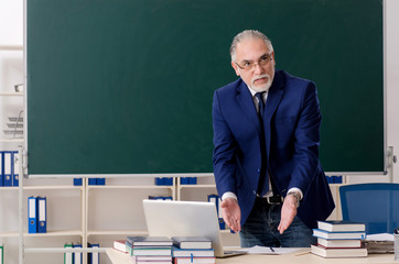 Aged male teacher in front of chalkboard 