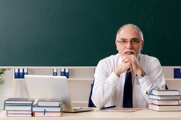 Aged male teacher in front of chalkboard 