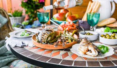 Fried fish on a plate. Dining table with different food and snacks. Seafood and vegetables. Summer lunch in the open air.