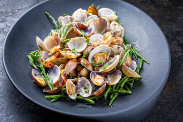 Steamed Japanese carpet shell with blanched green salicornia as closeup on a modern design plate