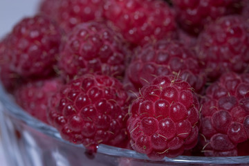 Close-up of a pile of juicy raspberries in a vase. The berries have a rich crimson color. The slightest hairs are visible.